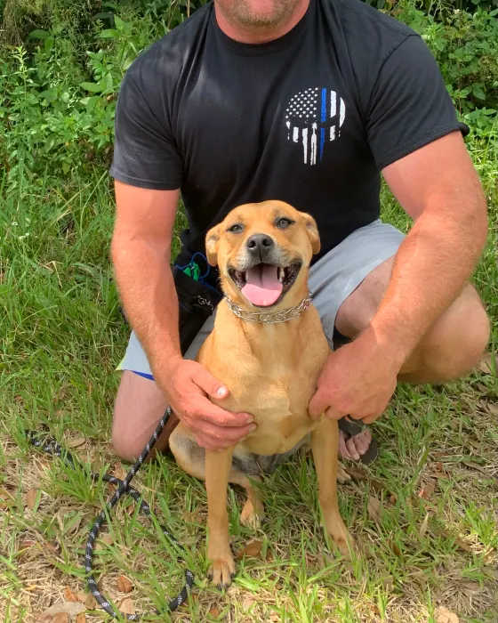 Chad Walker kneeling in a Florida yard beside a tan dog on a training lead