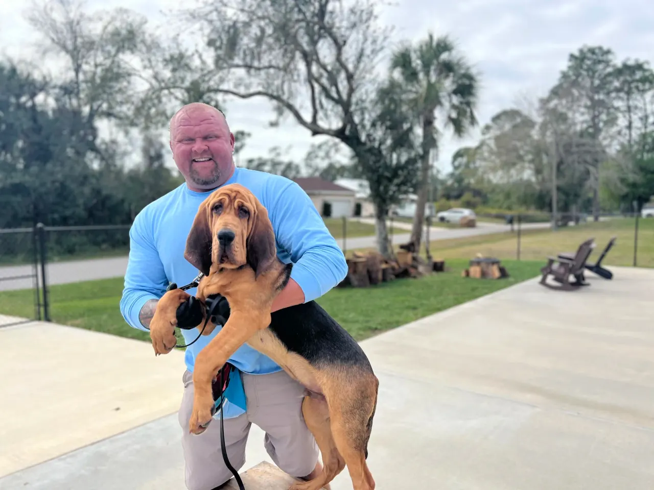Chad Walker crouching on a North Port driveway holding a bloodhound puppy