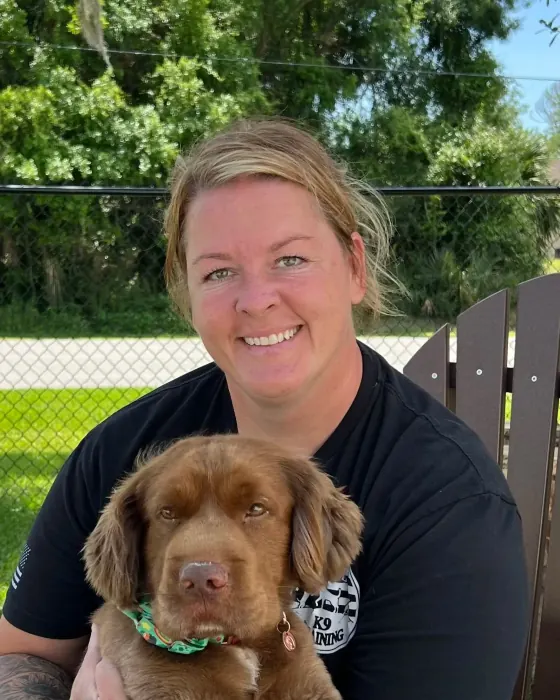 Kelly Walker holding a chocolate-brown puppy outside the training yard